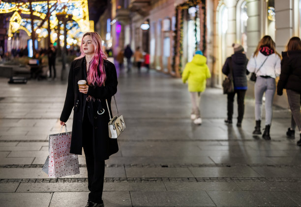 一个女人提着纸袋走在市区，享受着购物的乐趣。图片下载