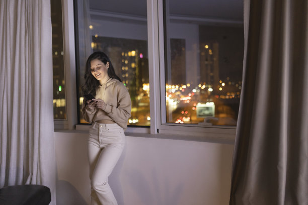 年轻女子在夜间使用智能手机的正面视图，背景是城市景观图片下载