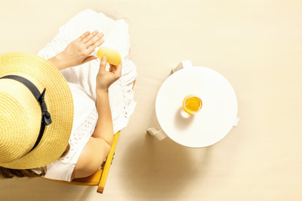 独自一人的女人用防晒霜保护皮肤，坐在沙滩桌旁喝橙汁。前视图。夏天图片下载