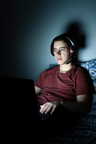 千禧一代躺在床上，关着灯在电脑上玩电子游戏图片下载
