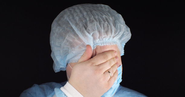 外科医生很沮丧，悲伤地闭上眼睛，把手放在黑色的孤立背景上。外科医生因辛苦工作而筋疲力尽。处理医生的想法会导致情绪崩溃。图片下载