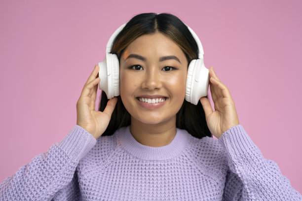 放松开朗的亚洲女子戴着无线耳机隔离在粉红色的墙上图片下载