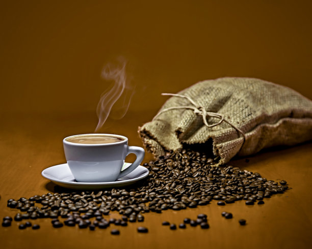 桌上的袋子里散落着咖啡豆，还有一杯热腾腾的浓咖啡图片下载