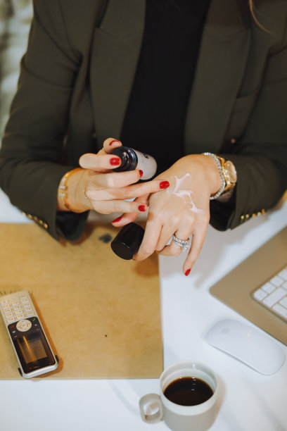 女性或男性的手在家庭办公室的笔记本电脑旁工作时，在手指上涂抹护手霜以滋润皮肤图片下载