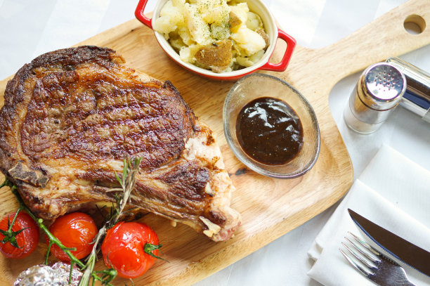 厚烤骨肋眼牛排与番茄和土豆泥在木托盘顶部视图图片下载