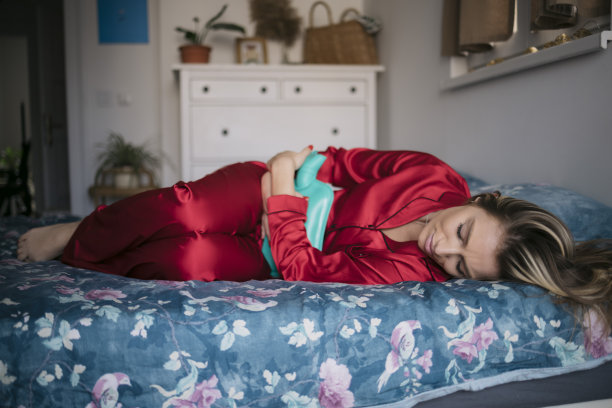 女人抱着热水瓶，在床上痛经图片下载