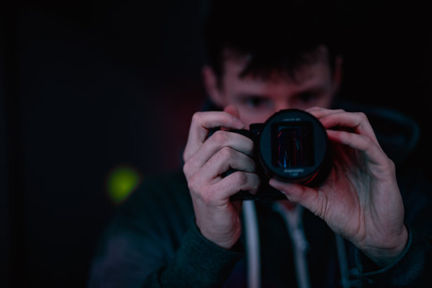 摄影师在室内霓虹灯色，人在专业相机设备上用变形镜头用紫色和粉色光拍摄。摄影师作为操作员，电影效果，生活方式概念摄影与选择性聚焦。图片下载