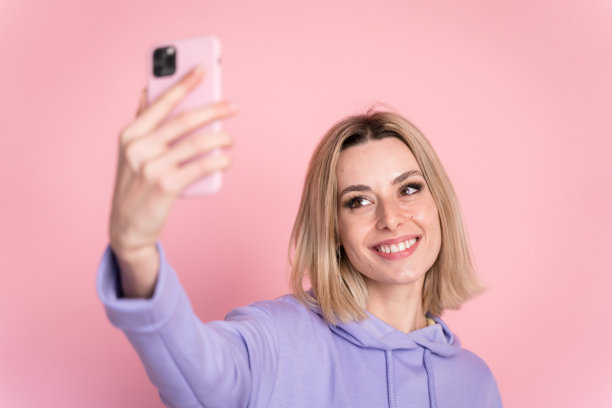 微笑的女人在工作室的粉红色背景上自拍图片下载