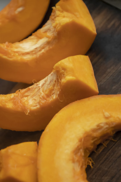 切好的南瓜放在木板上。桌子上放着一个切成小块的橘黄色南瓜。图片下载