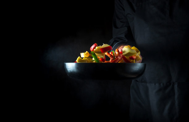 厨师在煎锅里准备蔬菜。在深色背景上烹饪健康的素食食物和餐点。免费广告位。图片下载