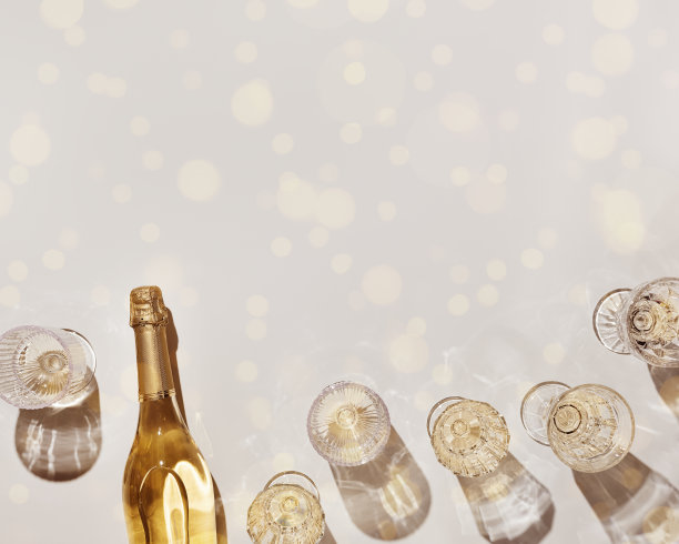 平铺白色起泡酒瓶，浅米色背景上有阳光阴影和闪光的酒杯。白酒审美照片，文案空间。暑假单色静物图片下载