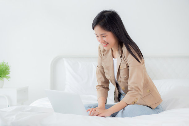 年轻漂亮的亚洲女人坐在床上使用笔记本电脑在卧室里在家工作，女性是自由职业者使用笔记本电脑在线，一个人，业务和生活方式的概念。图片下载