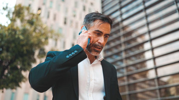穿着办公服，留着整齐胡子的中年商人正在使用手机。成功男士在智能手机上深情交谈。失望,麻烦图片下载