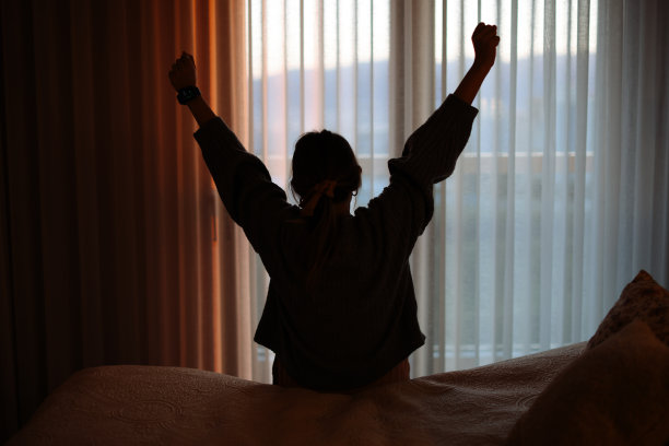 快乐的女人醒来后在床上伸展。快乐的年轻女孩迎接美好的一天。图片下载