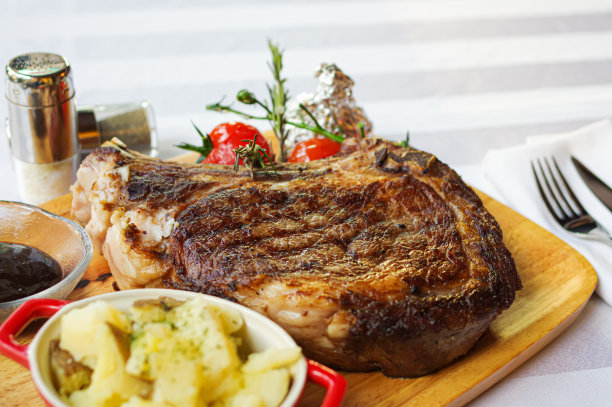 厚烤骨肋眼牛排配番茄和土豆泥，放在木托盘上图片下载