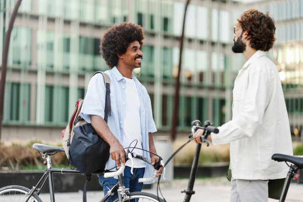 两个年轻的男性朋友骑着自行车在城市里聊天——环保通勤者图片下载