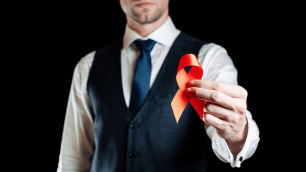 艾滋病的丝带。红丝带在艾滋病世界日在男子手中。黑色背景上的意识辅助和癌症符号。艾滋病毒，艾滋病和老龄化宣传月与复制空间。图片下载