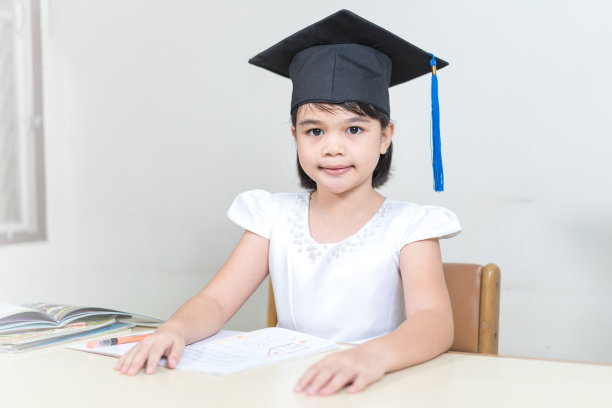 一个亚洲小女孩的肖像，戴着学士帽，坐在桌子旁图片下载