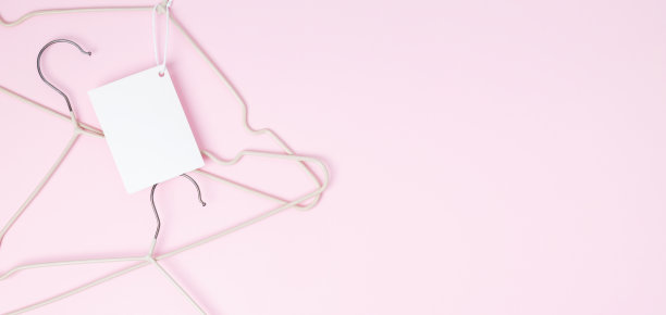 创意平铺衣架与白纸标签粉红色的背景。服装吊牌、标签空白模型模板。销售折扣店促销购物概念。前视图。本空间图片下载