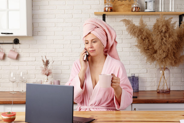 淋浴后穿着浴袍的女人在家庭办公室吃美味的甜点作为早餐。图片下载