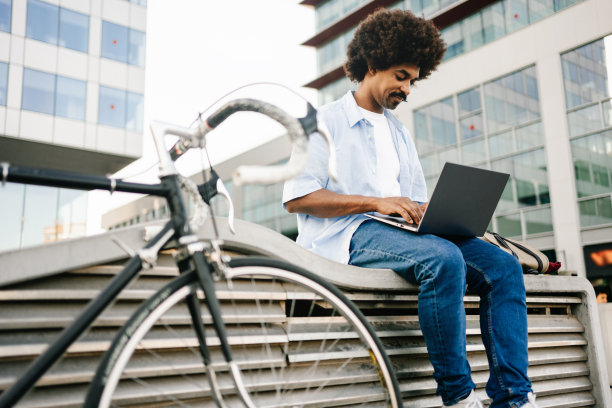 非裔美国自由职业者在笔记本电脑上工作-现代专业坐在户外与自行车图片下载