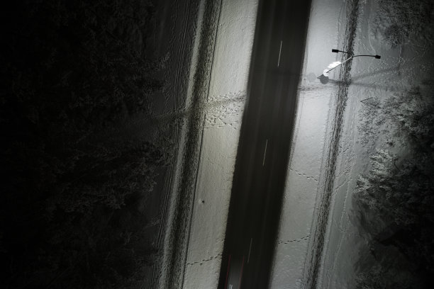 无人机拍摄的冬季道路在夜间蜿蜒穿过积雪覆盖的森林在山上图片下载