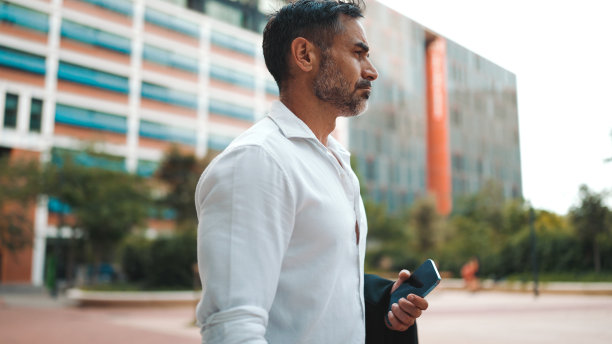 穿着白色衬衫，留着整齐胡须的成熟商人离开了位于城市金融区的办公室。成功人士辛苦工作一天后，手里拿着手机图片下载
