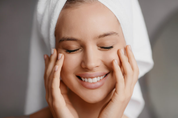 光亮肌肤和水疗护理。微笑的女士在毛巾触摸完美的脸与手，闭着眼睛摆姿势图片下载