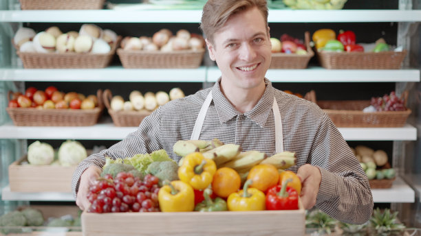 农民或企业主或创业企业家的肖像，站在商店里，提着装满新鲜水果和蔬菜的板条箱，自豪地微笑着有机农产品的健康食品。对工作肖像的骄傲。图片下载