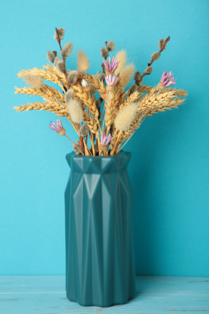 蓝色背景的花瓶里的干花。Verotical照片图片下载
