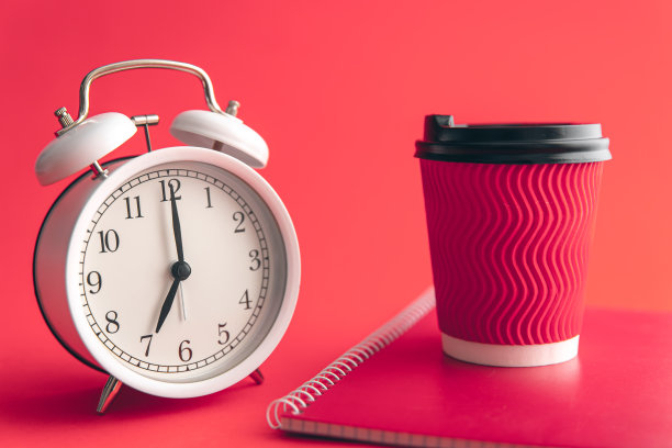 白色闹钟，纸杯和笔记本在模糊的背景。图片下载