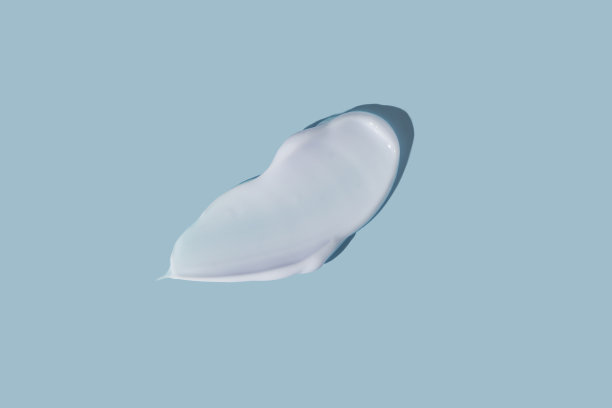 在蓝色背景上涂抹白色美容霜。乳状粉底纹理孤立。涂抹面霜。奶油质地的特写。图片下载