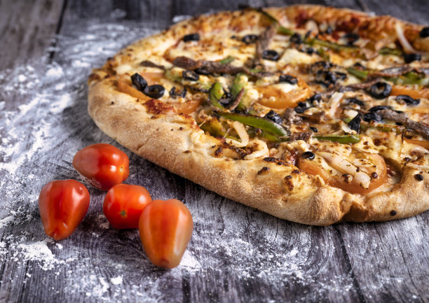 美味的意大利披萨放在经典的木桌上，蔬菜有番茄，胡椒，黑橄榄，凤尾鱼，块状图片下载