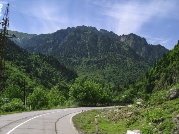 风景有一条路，在山上有绿色的灌木丛，树木和岩石山，阳光明媚的夏日图片下载