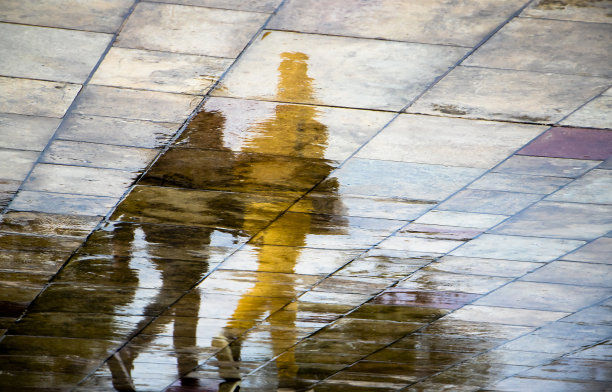 一个雨天，在潮湿的城市街道人行道上打着伞行走的无法辨认的人的抽象模糊剪影反射图片下载