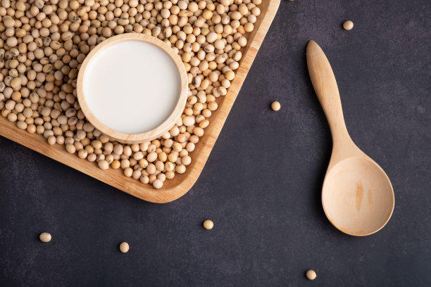 豆浆和黄豆放在木盘上，用大勺子舀。黑底黄豆。健康的即食食品。前视图。图片下载