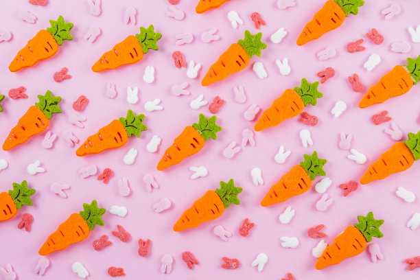 复活节图案的装饰与兔子耳朵糖洒和橙色胡萝卜在粉红色的背景。图片下载