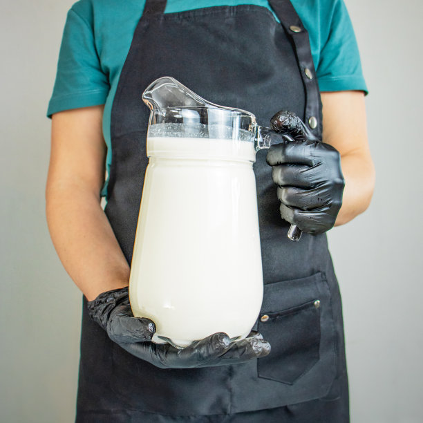 围着围裙戴着黑色手套的女人拿着一罐牛奶，特写，奶酪机，家用奶酪机图片下载