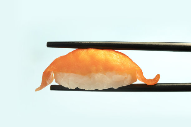 美味的寿司握寿司与鲑鱼清酒蓝色背景。日本传统料理。寿司在筷子在手特写。图片下载