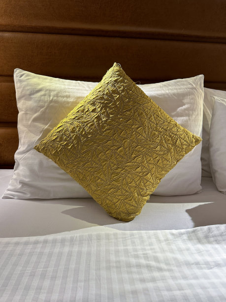 全帧图像堆叠的白色酒店枕头靠在人皮床头板，白色羽绒被床罩，金色靠垫，重点在前景图片下载