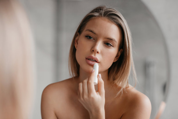 女性美容套路。迷人的女士用口红画她的嘴唇，在浴室里看镜子里的倒影图片下载