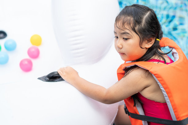 亚洲小女孩穿着救生衣坐在浮动环在游泳池。夏季休闲活动图片下载