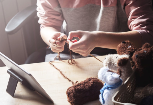 一名年轻女子坐在桌旁，用她的针织针编织，用剪贴板学习。图片下载