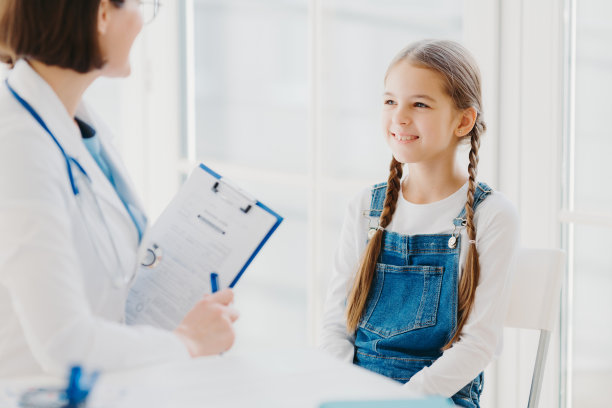 快乐的小孩认真听医生的建议和处方，来诊所看儿科医生，梳着两条小辫子，穿着牛仔工作服，谈论健康问题，进行体检图片下载