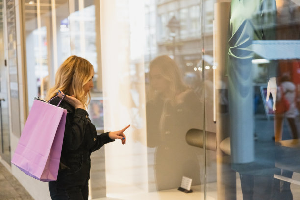 一个漂亮的金发女孩正在街上一家商店的橱窗里看衣服——广角镜头——日光图片下载