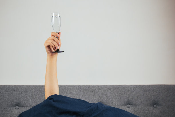 在床上男人手里拿着香槟。宿醉，酒精中毒的概念。节日的问候。图片下载