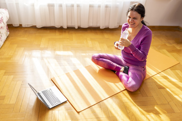 美女喝着水，在家里练习瑜伽，坐在瑜伽垫上冥想，微笑放松。图片下载