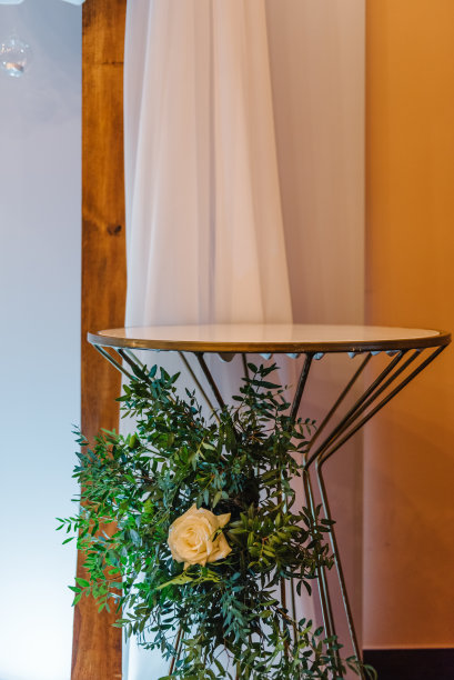 在拱门附近的桌子上用鲜花装饰着节日蛋糕。婚礼设置细节拱门或桌子。装饰细节。宴会厅餐厅的花卉和绿色植物。接待,设置。特写镜头。图片下载