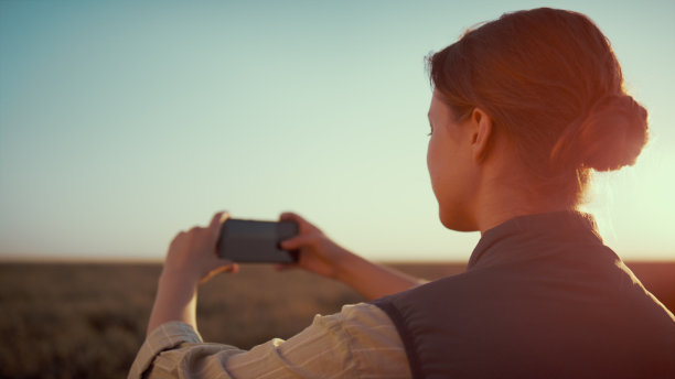 女子在金色的阳光下拍摄麦田。秋天是农耕季节。图片下载