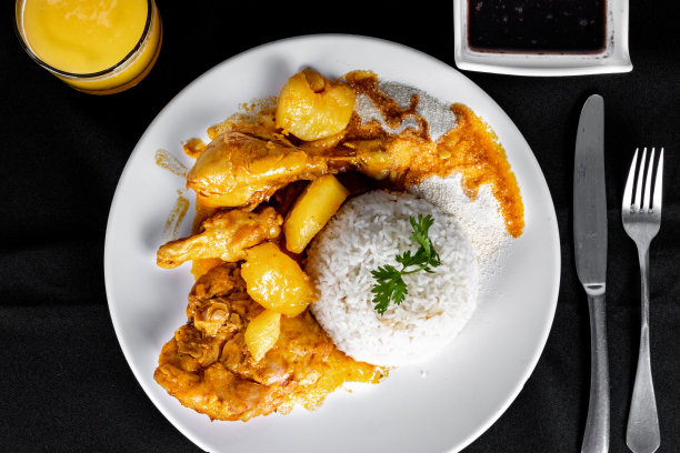 自制鸡肉炖西红柿、洋葱和土豆，放在黑色布质桌子上，盘子里放着米饭、豆子和橙汁图片下载